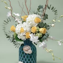 Yellow roses and white hydrangeas in a blue vase with shell accents