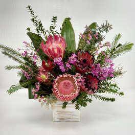 Pink protea and small magenta blooms arranged in a rustic white wooden cube container