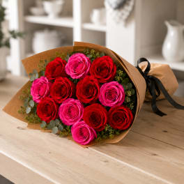 Bouquet of red and pink roses wrapped in brown paper with a black ribbon