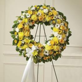 Standing wreath of yellow and white flowers with a white bow on a metal easel.