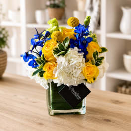 Bouquet of yellow roses, white hydrangeas, and blue flowers in a glass vase