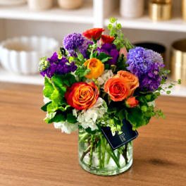 Mixed bouquet of roses, hydrangeas, and purple blooms in a glass vase