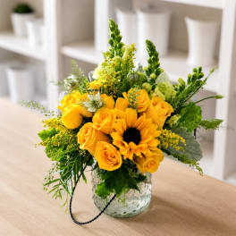 Yellow roses and a sunflower in a clear glass vase