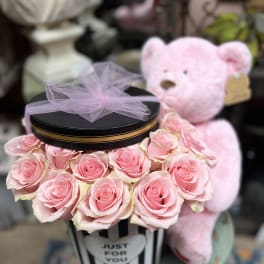 Pink roses arranged in a striped gift box with a teddy bear behind it