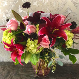 Pink roses and red lilies in a glass vase with green hydrangeas