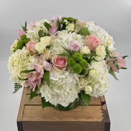 Round bouquet of white hydrangeas, pink roses, and green button mums in a glass vase