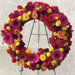 Bright circular wreath of red, pink, yellow, and orange flowers on a black easel stand