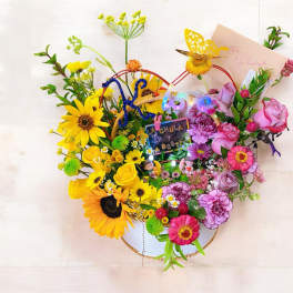 Colorful basket arrangement with yellow sunflowers and roses on one side and pink roses and carnations on the other.