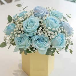Blue roses arranged in a yellow box with baby's breath