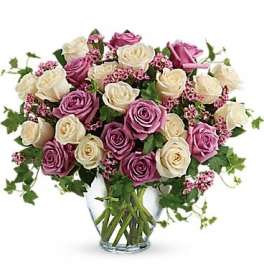 Pink and white roses in a clear glass vase with trailing greenery