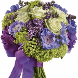 Bouquet of pale roses, purple flowers, and green blooms tied with a purple ribbon