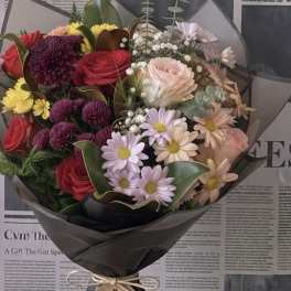 Mixed bouquet of roses and daisy-like flowers wrapped in black paper