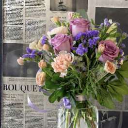 Bouquet of pink roses, peach carnations, and purple filler flowers in a glass vase