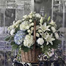 Basket arrangement of white lilies, roses, and hydrangeas with a blue hydrangea cluster