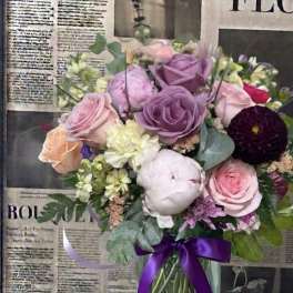 Mixed bouquet of pink, purple, and white flowers in a glass vase with a purple ribbon