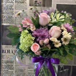Mixed pink and purple bouquet in a glass vase with a purple ribbon