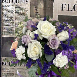 Bouquet of white, lavender, and purple roses in a glass vase with a purple ribbon
