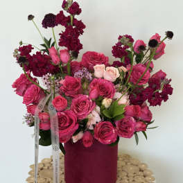 Pink and magenta roses arranged in a round box with ribbon.