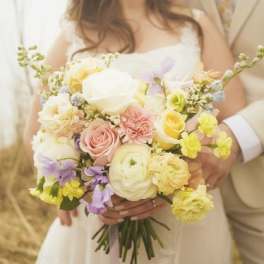 Bride holding a pastel bouquet of roses, ranunculus, and small blooms