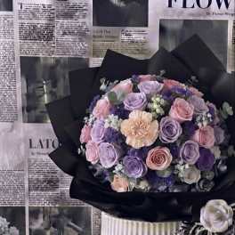 Bouquet of pink and lavender roses with a peach carnation in black wrap