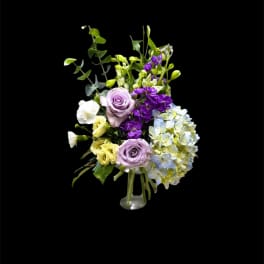Lavender roses, hydrangea, and purple flowers in a clear vase
