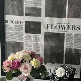 Pink and white flower bouquet in a glass vase beside a small gift box with ribbon.