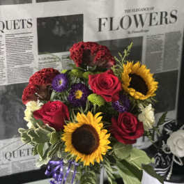 Mixed bouquet with sunflowers, red roses, and purple blooms in a glass vase