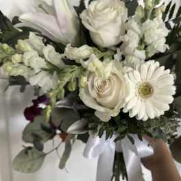 White bouquet with roses, lilies, and a gerbera daisy tied with a satin ribbon