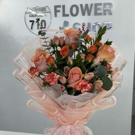 Bouquet of peach and pink roses with red carnations in pink wrap