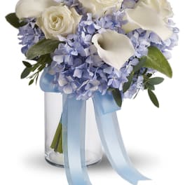 White roses and calla lilies in a glass vase with blue hydrangeas