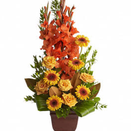 Tall arrangement of orange flowers and yellow daisies in a brown vase