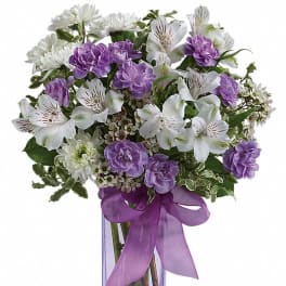 Purple and white bouquet in a clear square vase with a purple ribbon