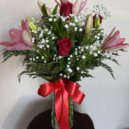 Pink lilies and red roses in a glass vase with a red ribbon