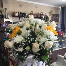 Large white and yellow flower arrangement in a glass vase with a white ribbon