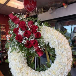 Heart-shaped floral wreath with red roses and white flowers on an easel