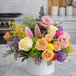 Pastel flower arrangement with roses and bunny ears pick in a white cylinder vase