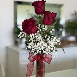 Three red roses in a glass vase with white baby's breath and a red ribbon