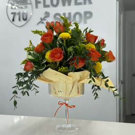 Orange roses and yellow mums in a stemmed glass vase with ribbon