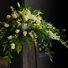 White floral arrangement with cascading greenery on a dark pedestal