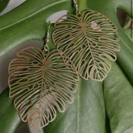 Pair of gold leaf-shaped dangle earrings on a green leaf background