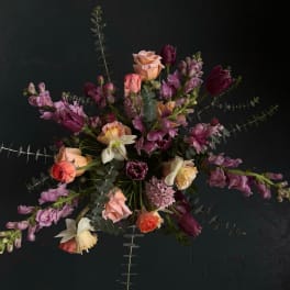 Moody arrangement of peach roses, white daffodils, and purple tulips on a dark background