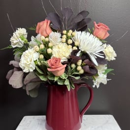 Pink roses and white flowers arranged in a burgundy pitcher vase