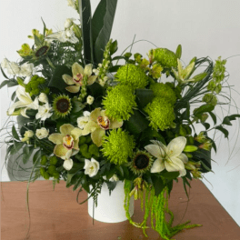 Green and white floral arrangement in a white vase with orchids and lilies