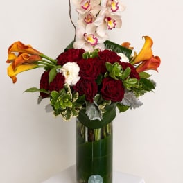 Red roses and calla lilies with white orchids in a tall glass vase