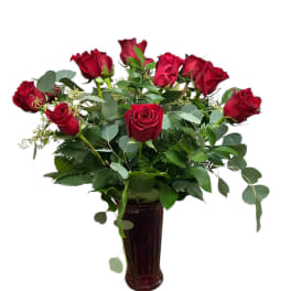 Red roses arranged in a tall dark vase with greenery