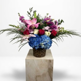 Mixed bouquet with pink lilies, roses, and blue hydrangea in a woven basket