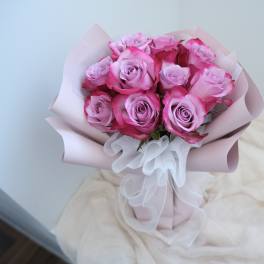 Bouquet of pink roses wrapped in pale pink paper with a white ribbon