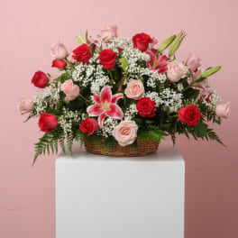 Basket arrangement of red and pink roses with lilies on a pink background