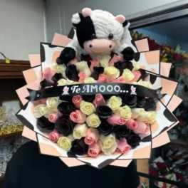 Bouquet of pink, cream, and black roses with a plush cow topper