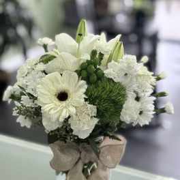 White floral bouquet in a clear glass vase with a burlap bow